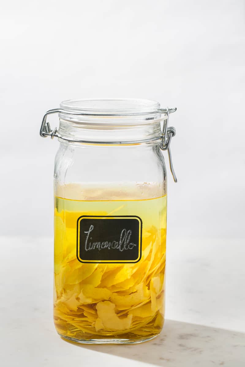 glass jar filled with vodka and lemon peels with a handwritten limoncello label