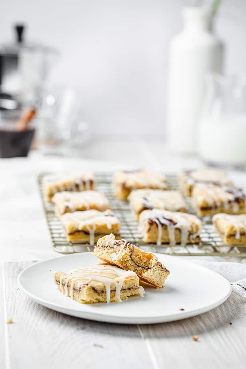 glazed cinnamon roll bars in the background with two on a plate in front