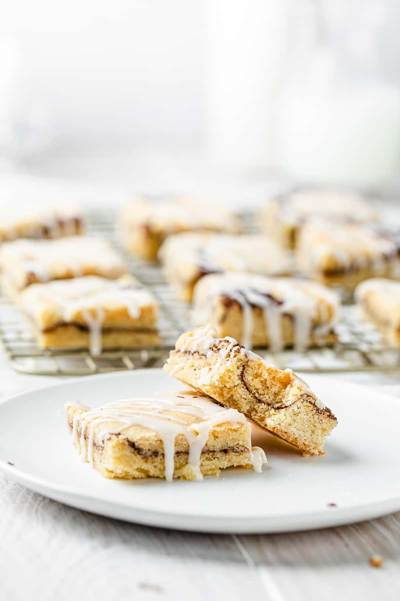 glazed cinnamon roll bars in the background with two on a plate in front
