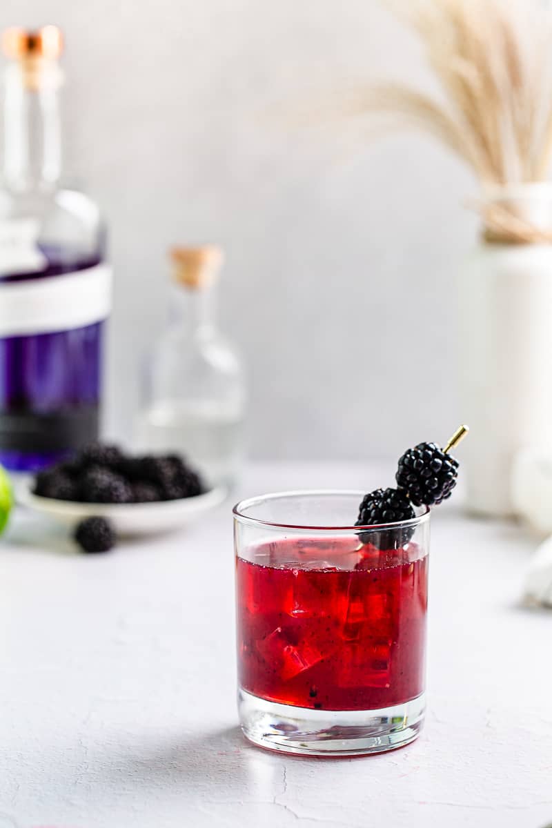Blackberry Empress Gin Sour on the rocks with blackberry garnish, with Empress Gin bottle in the background