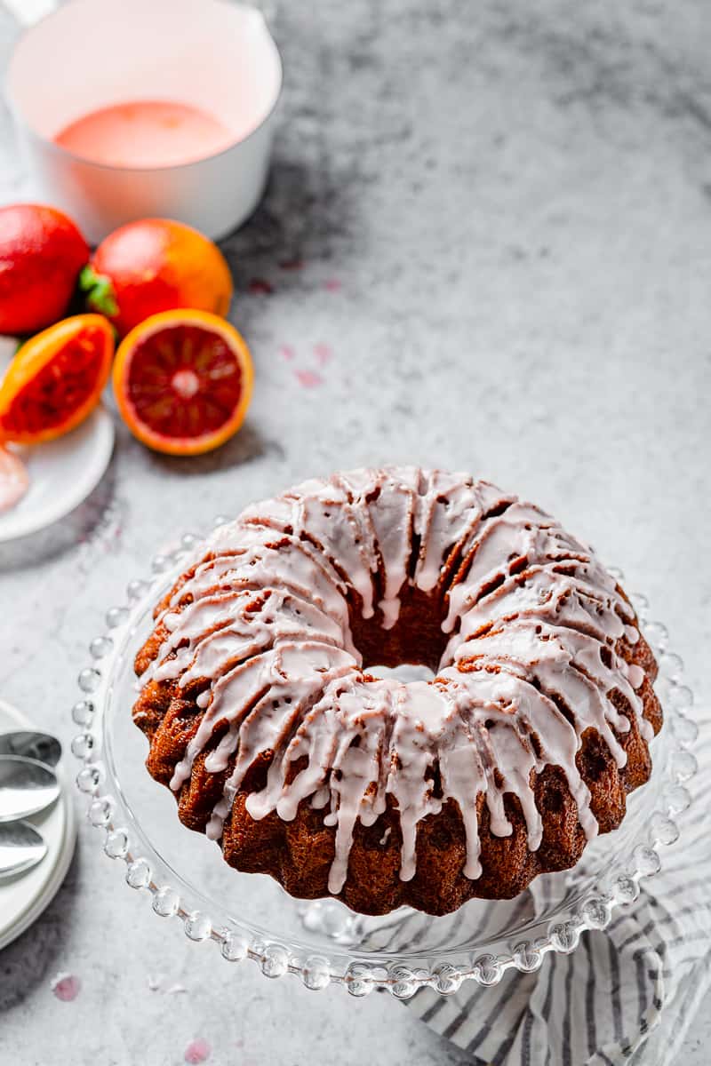 blood orange pound cake on a cake stand with blood oranges in the background