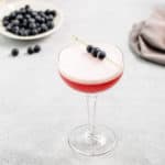 Blueberry Gin Sour in a coupe glass with blueberries in the background