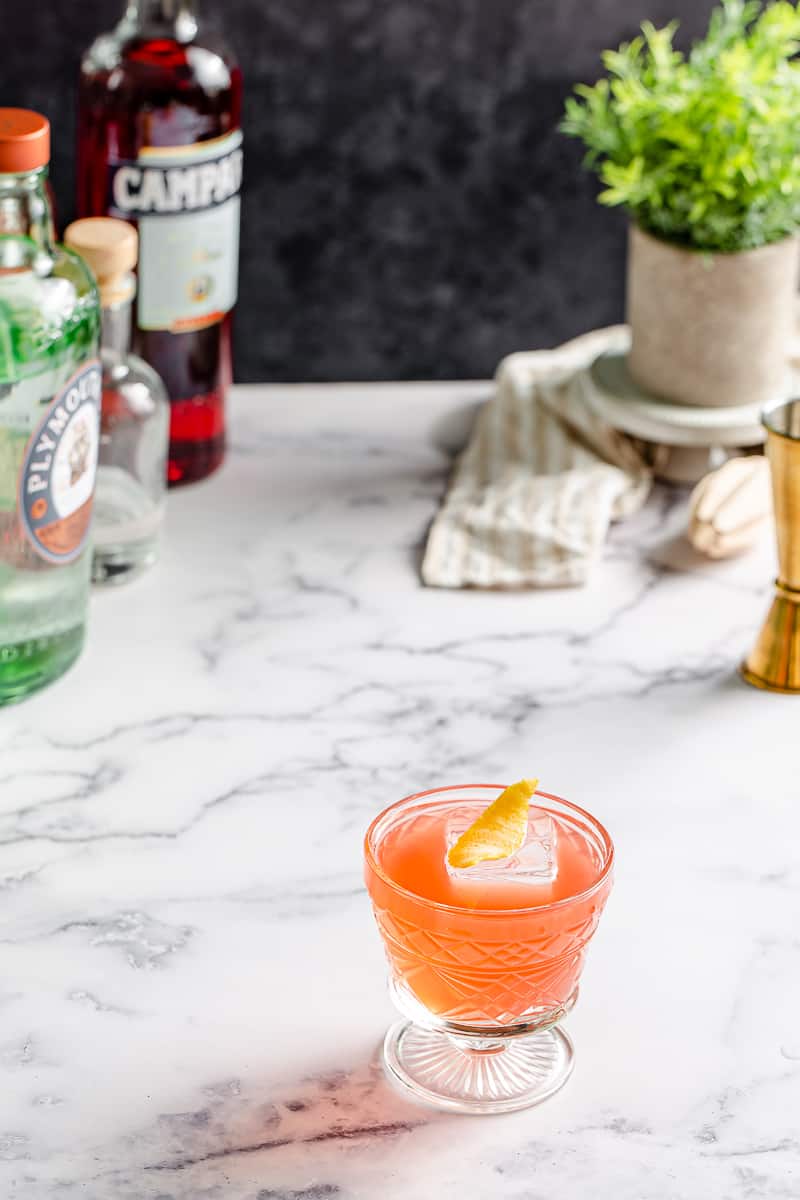 gin campari sour with bottles and accessories in the background