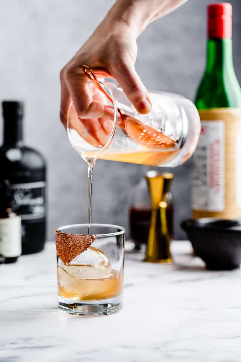 pouring mezcal cocktail over a sphere of ice