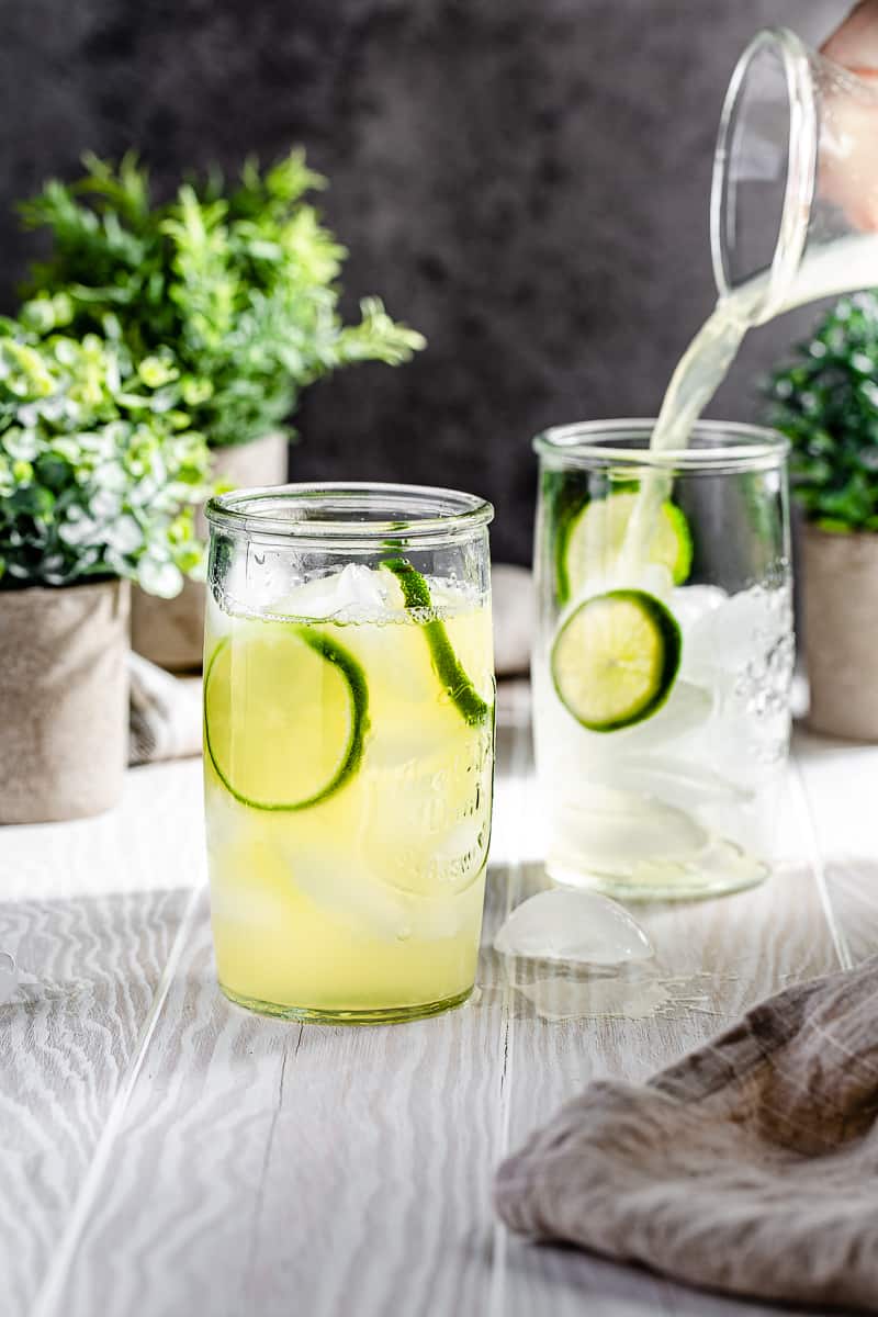 pouring pineapple limeade into serving glass that has lime wheels