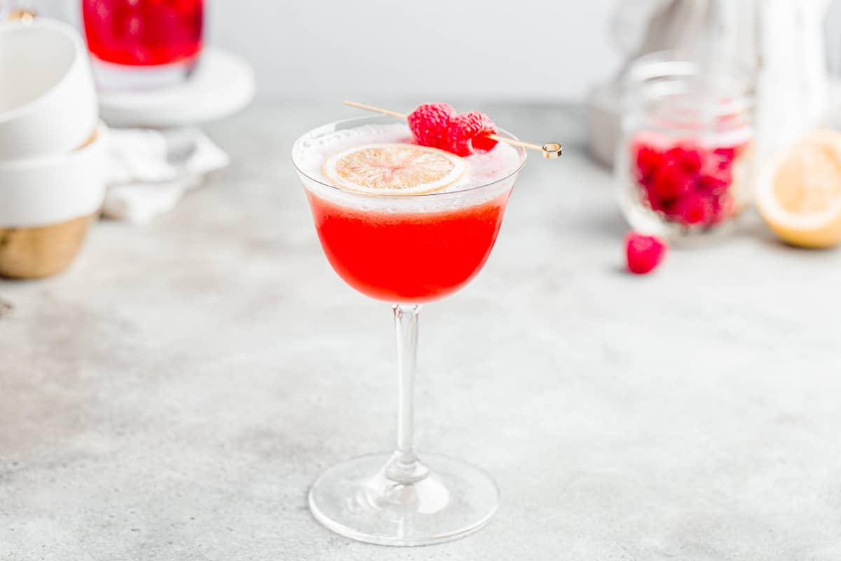 horizontal image of raspberry mocktail with teacups, raspberries, and lemons in the background