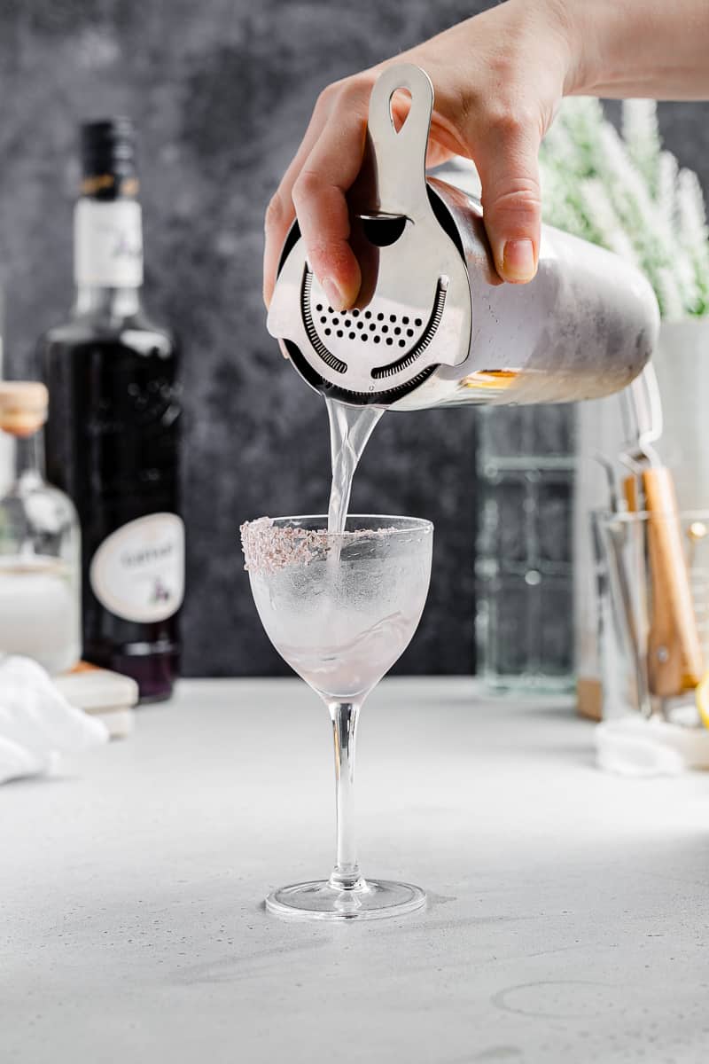 pouring cocktail into a chilled glass with a sugar rim