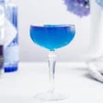 blue cocktail in a coupe glass with a purple layer on top