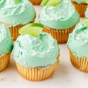 close up shot of a group of margarita cupcakes with lime wedges on top