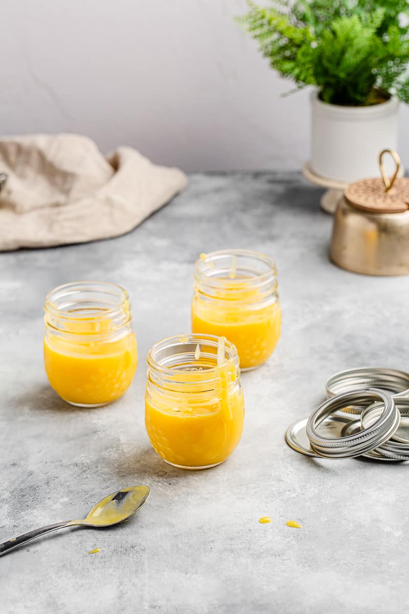 three jars of lemon curd on a table with a plant in the background