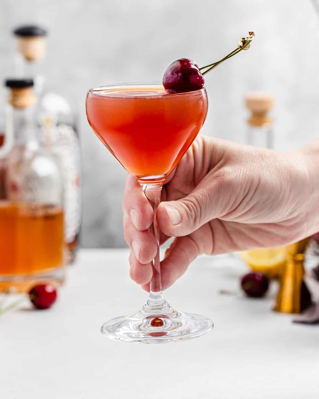 hand picking up cocktail glass with cherry garnish