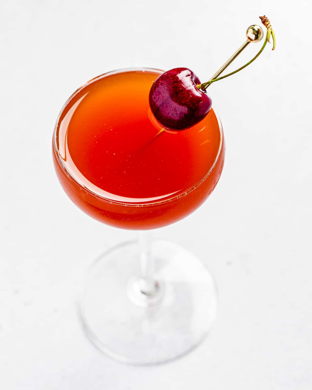 close up top view of red cocktail with a fresh cherry garnish