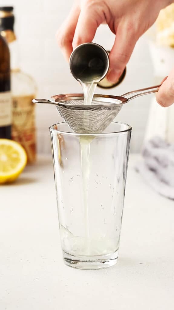 pouring lemon juice through a strainer into the cocktail mixing glass