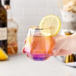 cocktail in an iridescent glass held in a hand with lemon wheel garnish