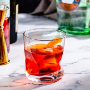 Close up of a Negroni cocktail, a red-colored drink in an old fashioned glass with a large piece of orange peel