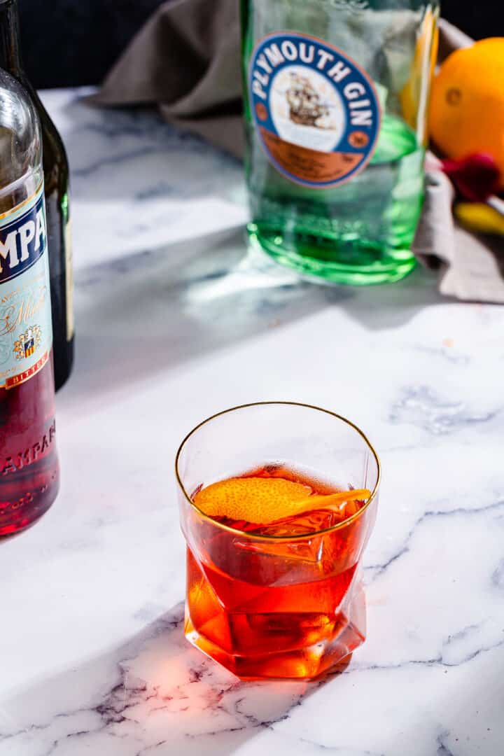 red Negroni cocktail on a marble tabletop with alcohol bottles in the background