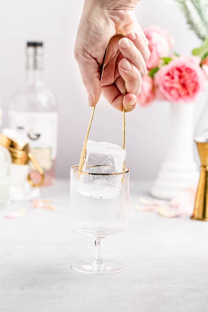 adding large clear ice to gold-rimmed cocktail glass