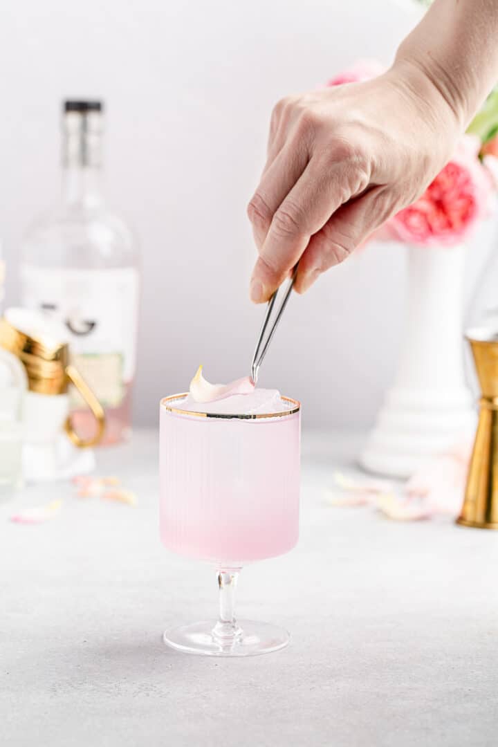 adding rose petal garnish to a pink cocktail
