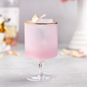 pink empress gin cocktail with rose petal garnish in a gold-rimmed footed cocktail glass
