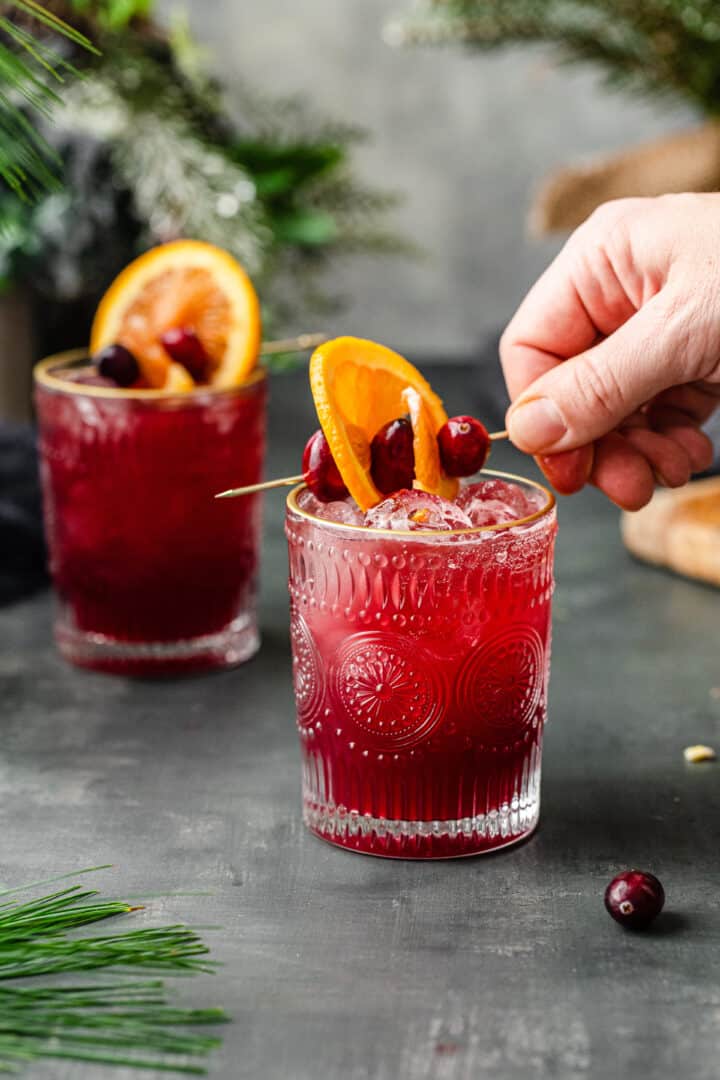 adding an orange and cranberry garnish to mocktail