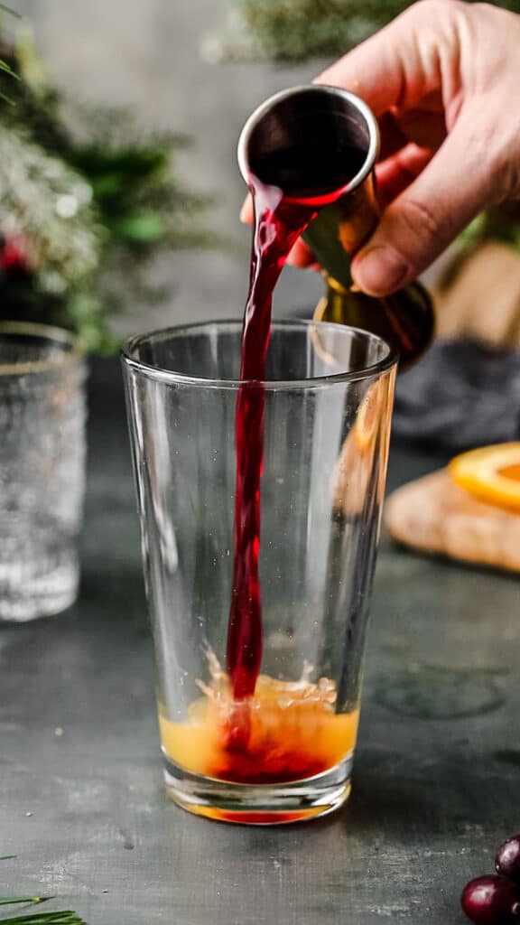 pouring cranberry juice into a cocktail shaker