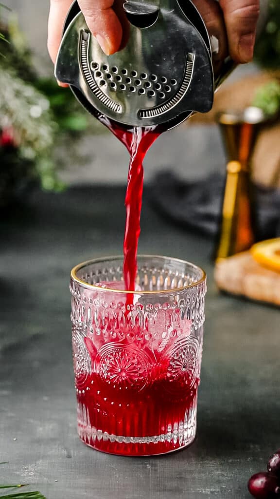 straining cranberry and orange juice mocktail into the serving glass