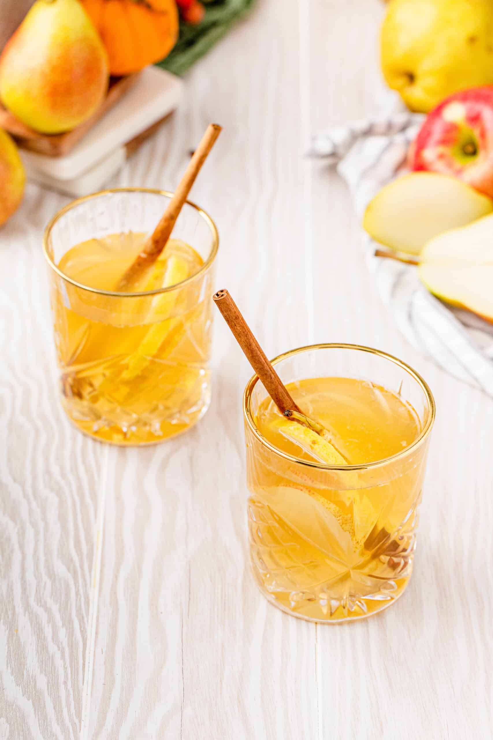 Two glasses of white wine sangria on a countertop. The Drinks are garnished with fruit and cinnamon sticks.