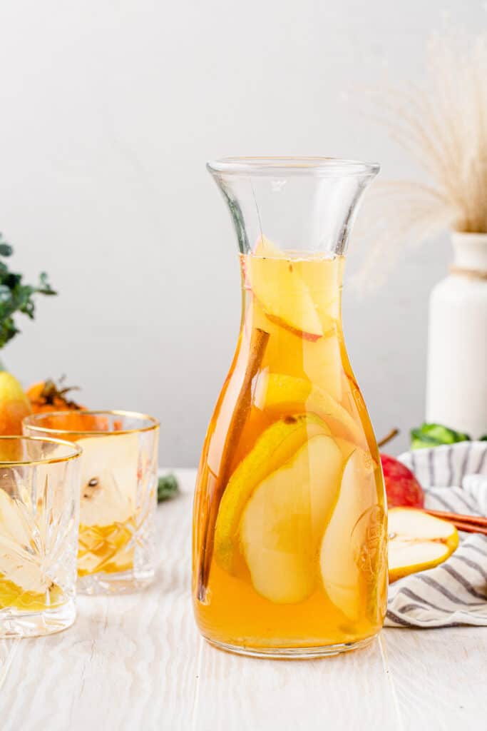 fall sangria with apple cider in a pitcher with serving glasses next to it