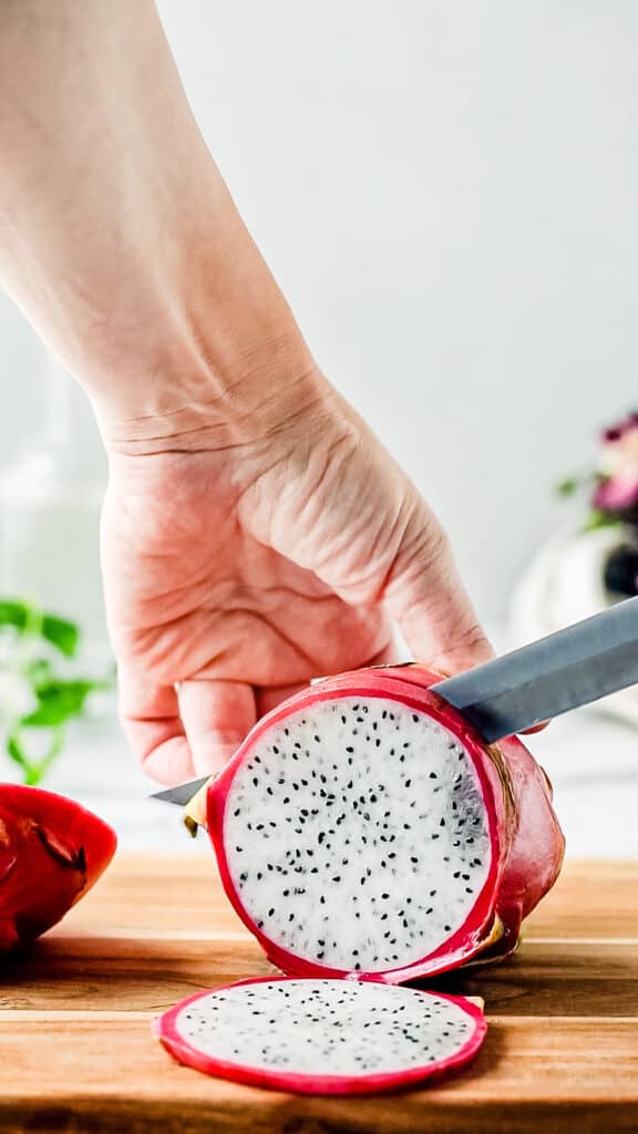 Hands with a knife cutting into a dragon fruit
