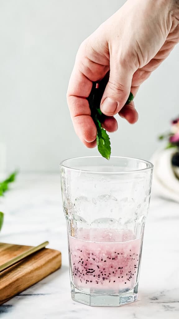 Hand dropping fresh mint into a cocktail glass.