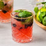 Two ginger beer bitters mocktails with lime, blueberry and mint garnish, with mint and limes in the background.