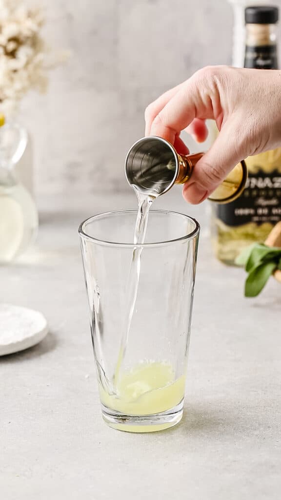 Adding the sage syrup to the cocktail shaker.