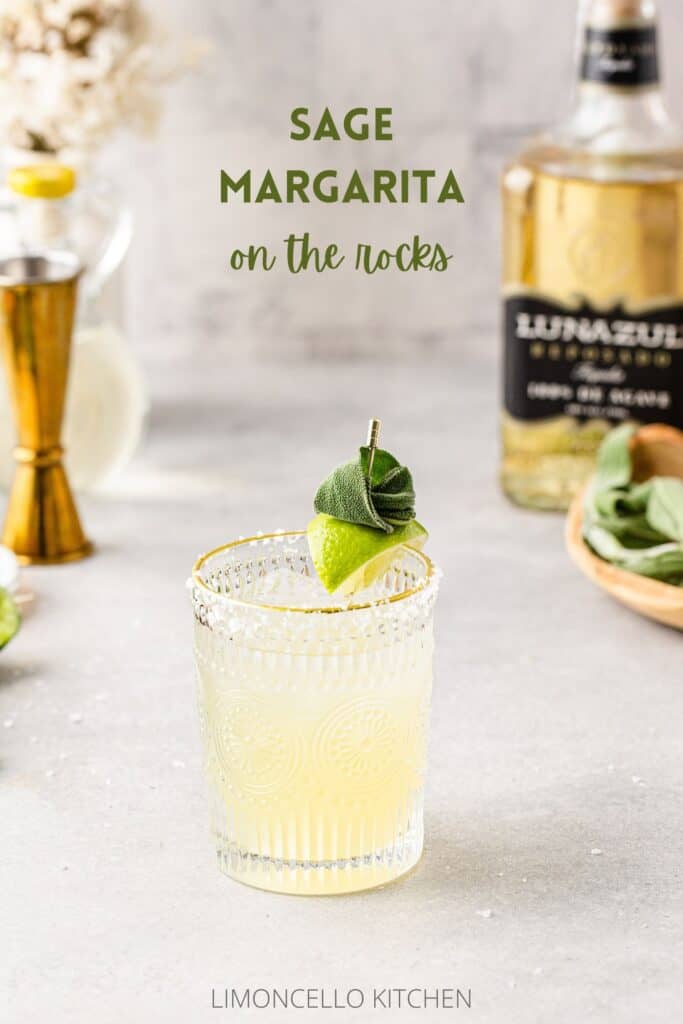 Margarita in a glass with lime and sage garnish, and with a jigger and tequila bottle in the background.