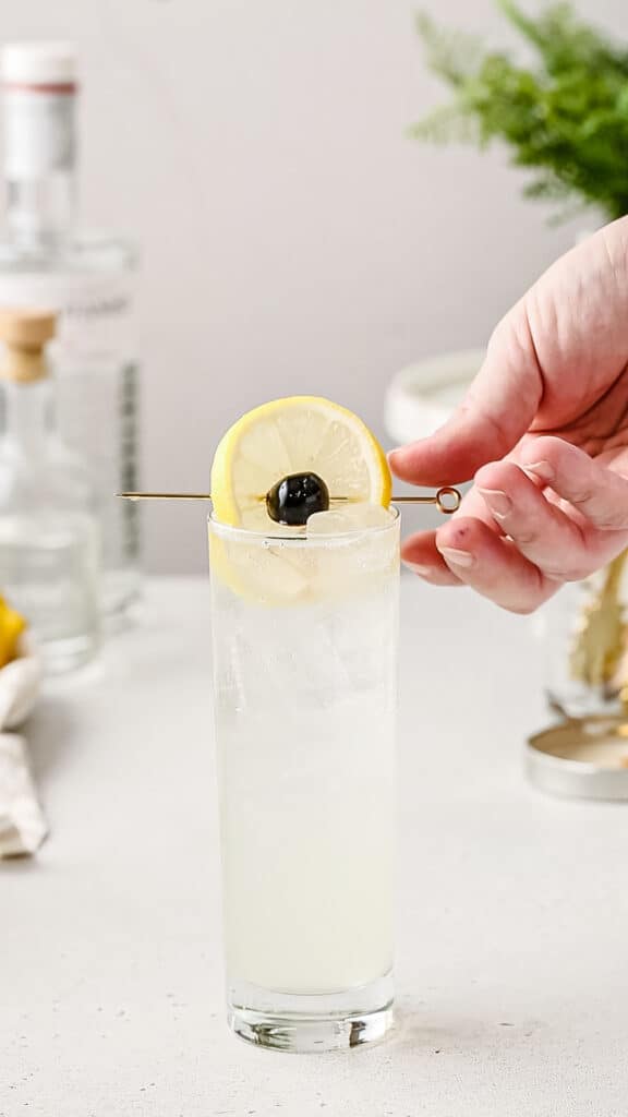 hand placing the lemon and cherry garnish on the cocktail glass.