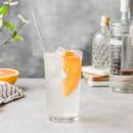 Side view of tall grapefruit rickey cocktail with a glass straw and half a grapefruit slice.