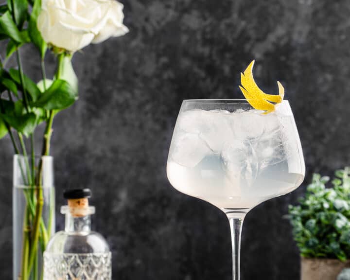 Side view of cocktail with lemon peel garnish with white roses in the background.