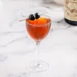 LIttle Italy cocktail in a Nick and Nora cocktail glass with two maraschino cherries on a cocktail pick resting on top of the drink.