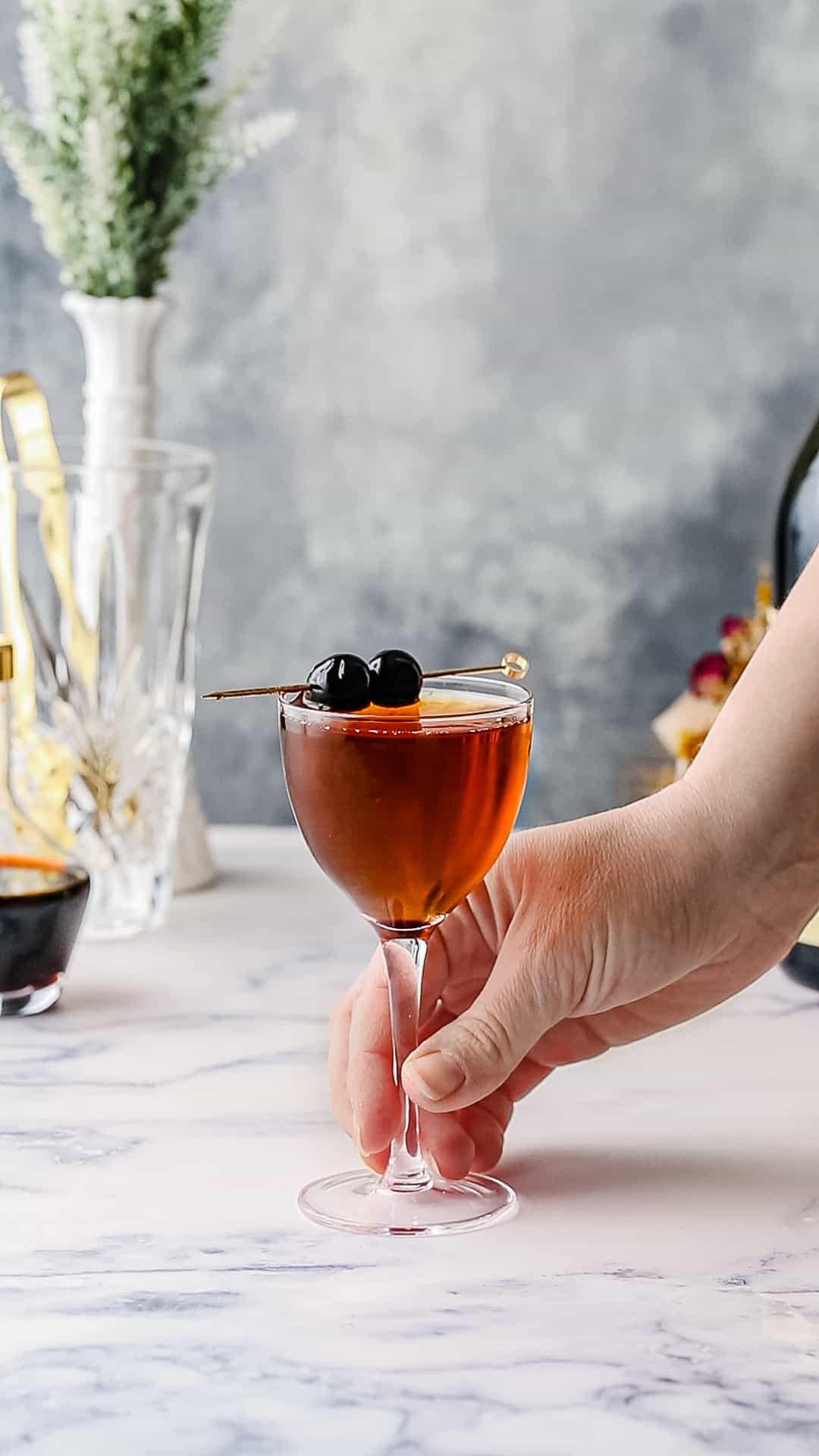 Hand holding the stem of a cocktail with a double cherry garnish.