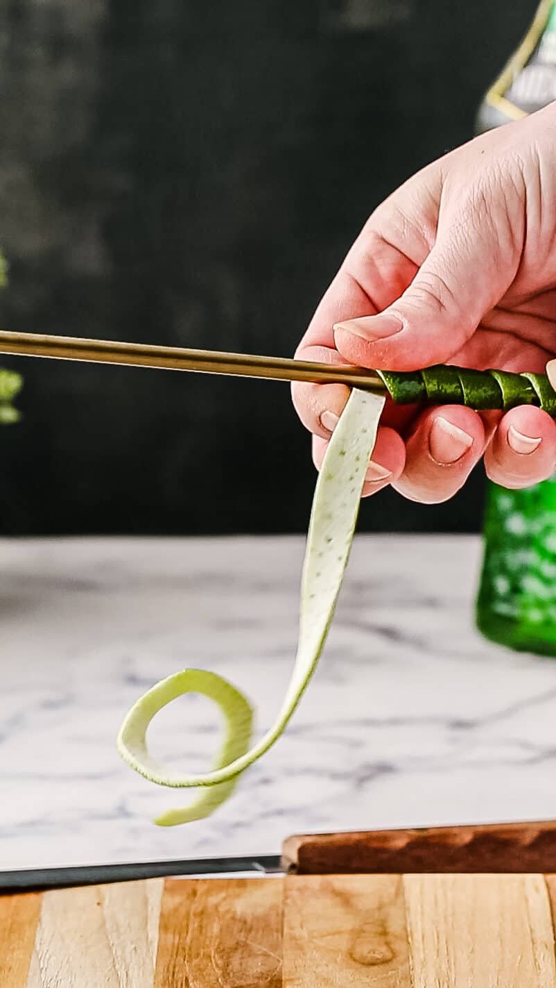 Twisting the lime zest strip around the handle of a bar spoon.
