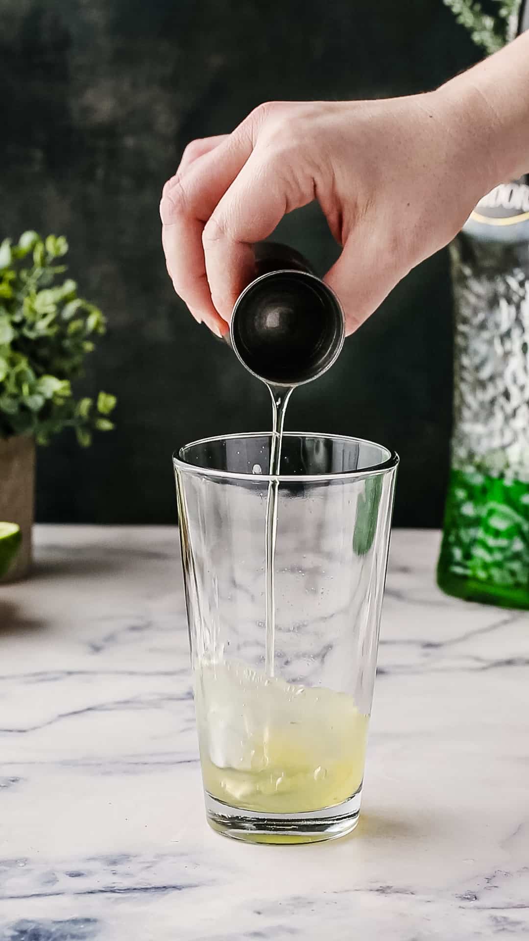 Hand pouring egg white from a jigger into a cocktail shaker.