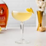 Side view of Amaretto French 75 cocktail with Amaretto bottle and jigger in the background.