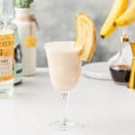 Banana Cow cocktail with a quartered banana as a garnish on a tabletop with ingredients and bar tools in the background.