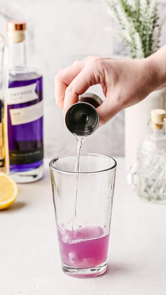 Adding simple syrup from a cocktail jigger into a cocktail shaker.