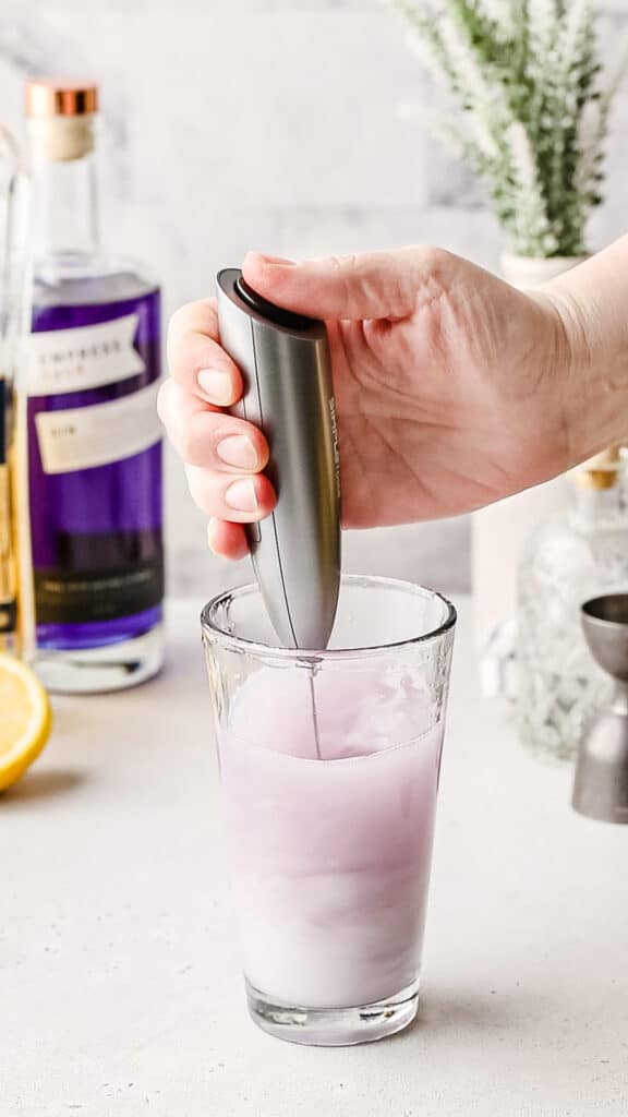 Using a milk frother to mix a gin fizz cocktail.