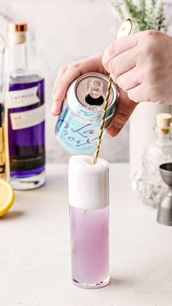 Pouring seltzer along the bar spoon in a gin fizz.