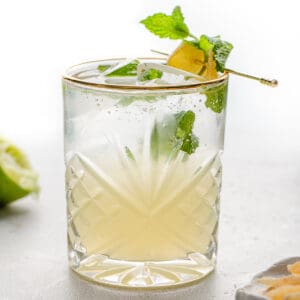 Side view of Gin Gin Mule on a white background with a lime and candied ginger.