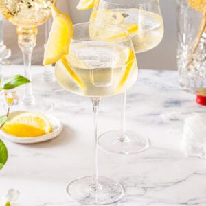 Two Amaro Spritz cocktails on a marble countertop with lemon slices and a lemon wedge garnish.