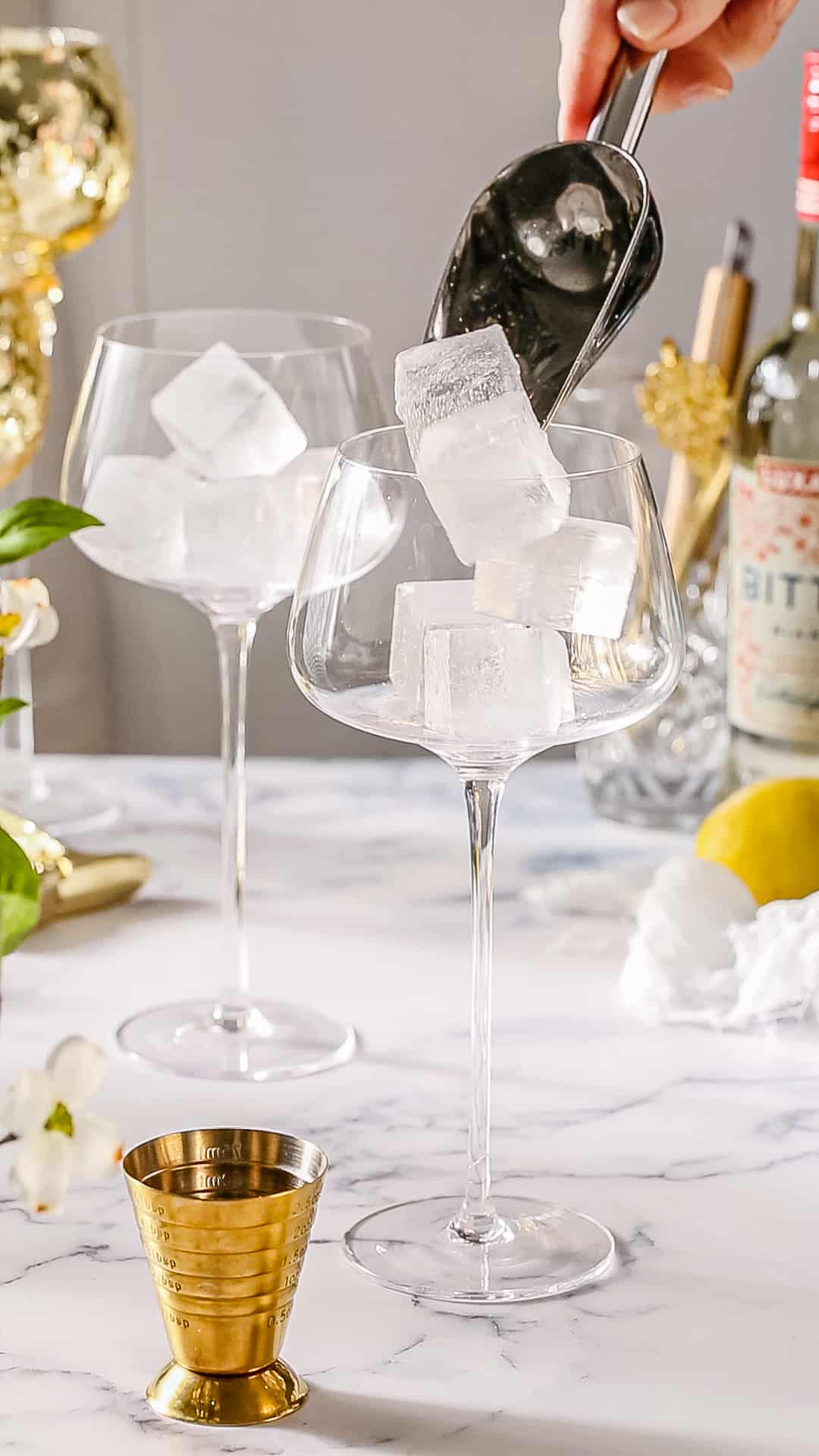 Hand adding ice to a cocktail glass using an ice scoop.