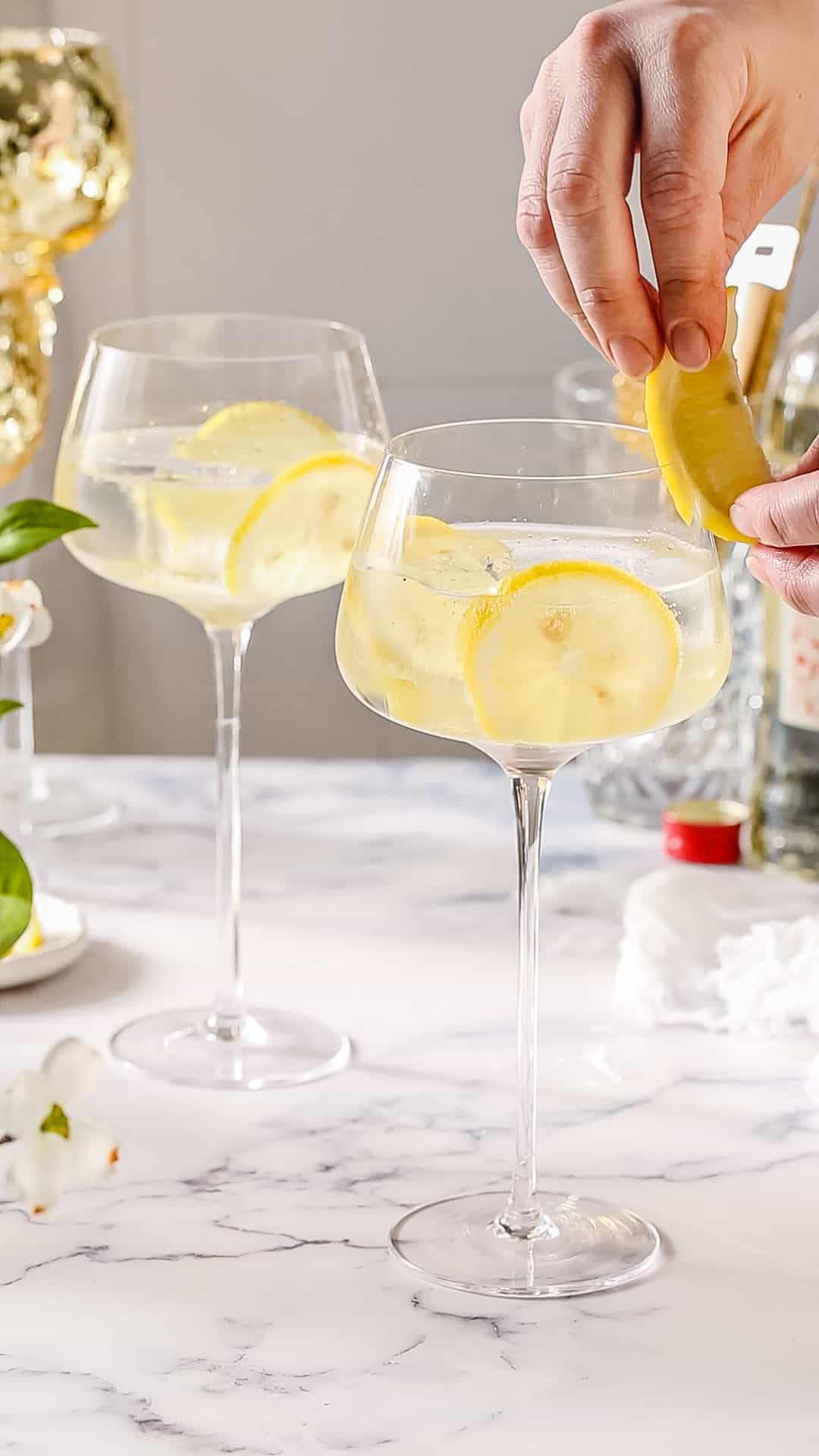 Hand adding a lemon wedge garnish to a cocktail glass.