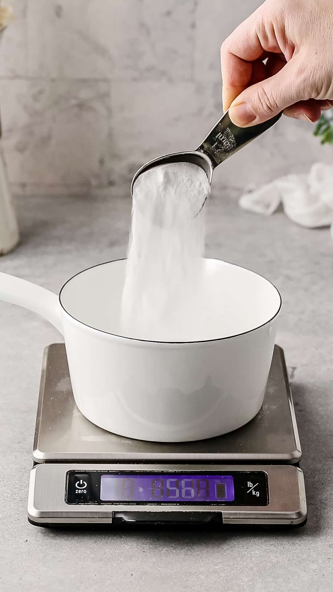 Pouring sugar into a saucepan and weighing it on a food scale.